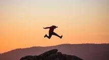 A person jumping at the top of a mountain on a sunset landscape.
