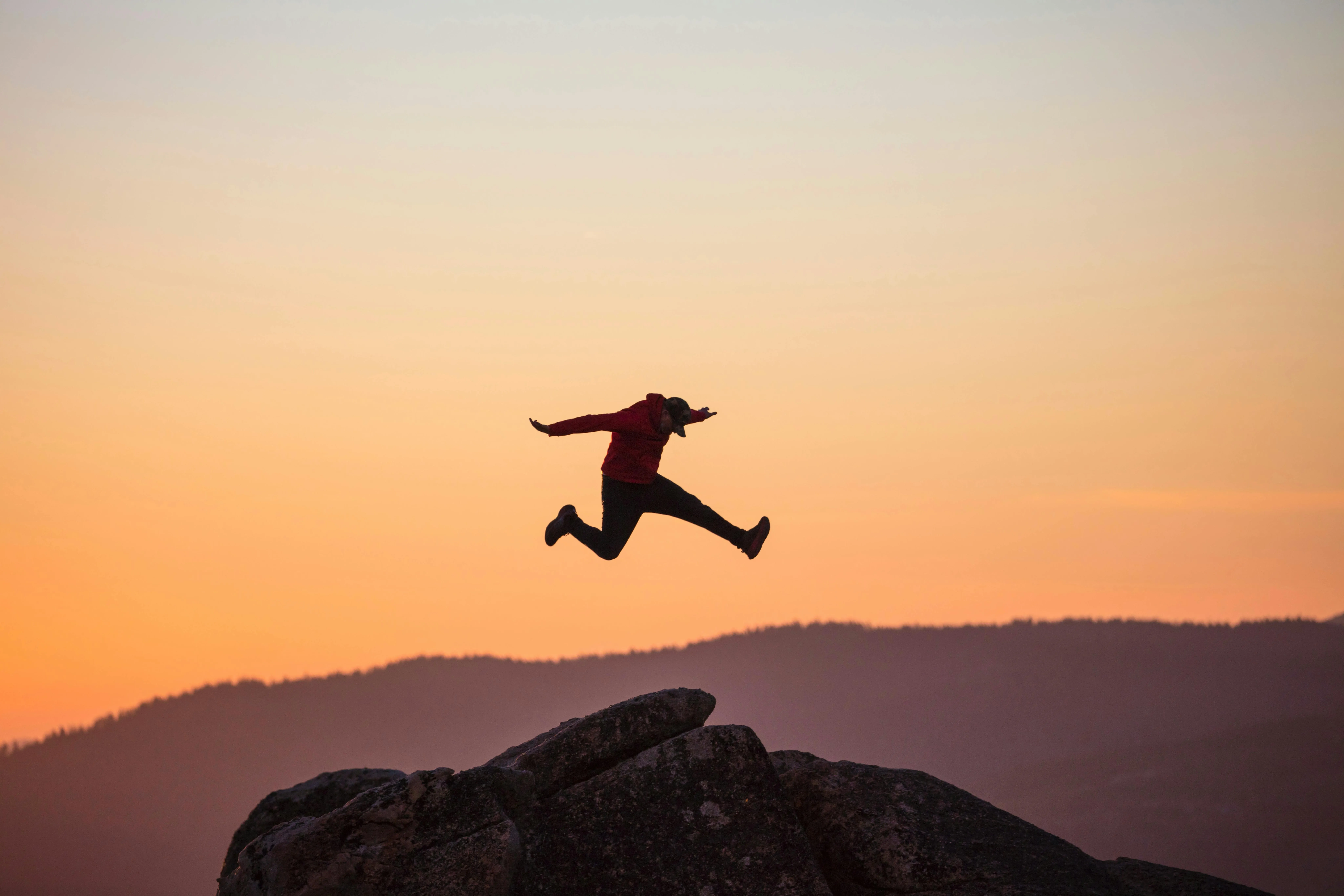 A person jumping at the top of a mountain on a sunset landscape.