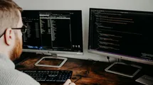 A software developer working with two monitors on a wooden desk.