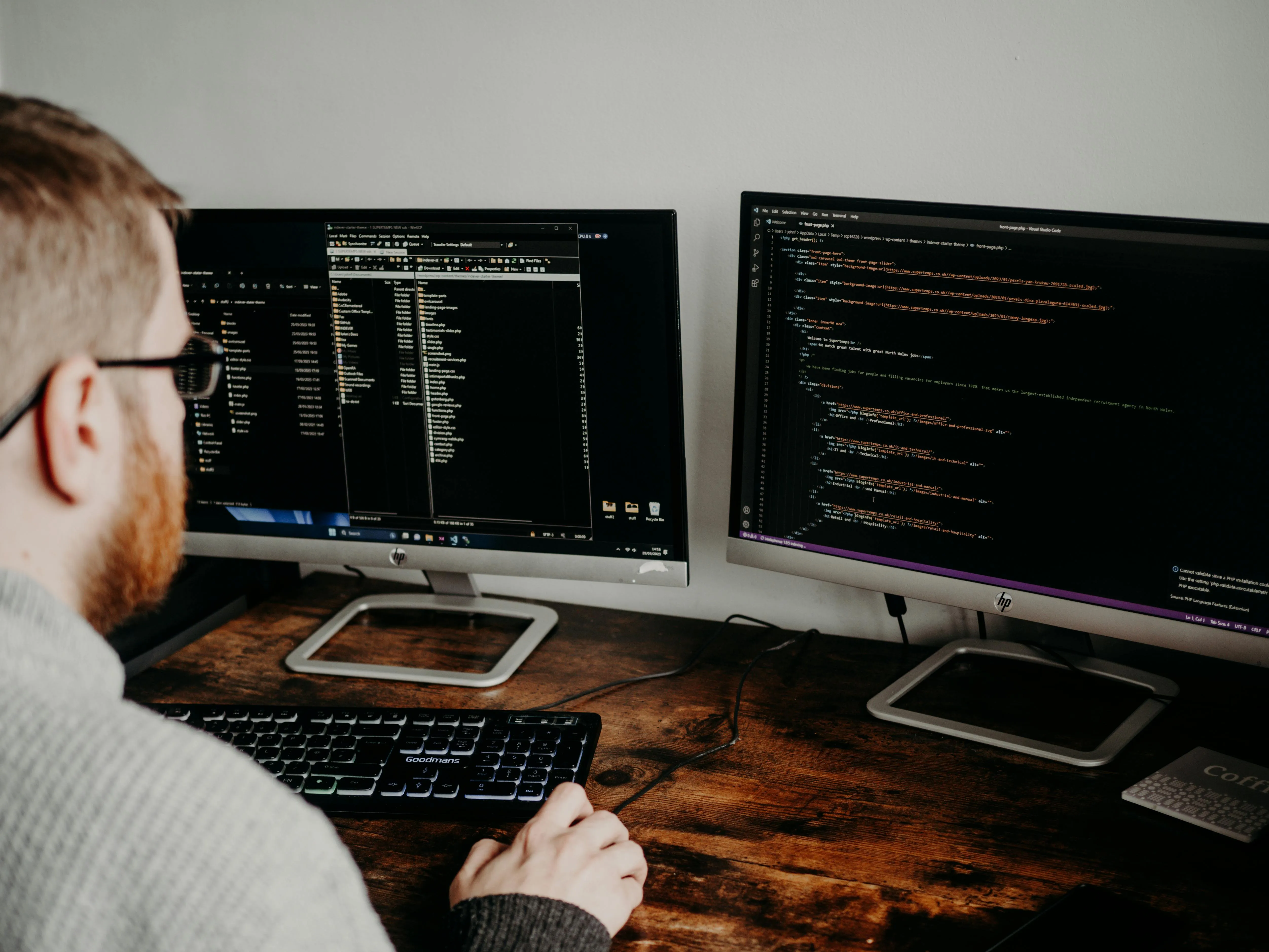 A software developer working with two monitors on a wooden desk.