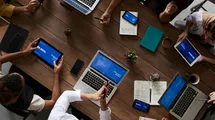 A photo taken from above showing a meeting table with people woriking with their laptops.