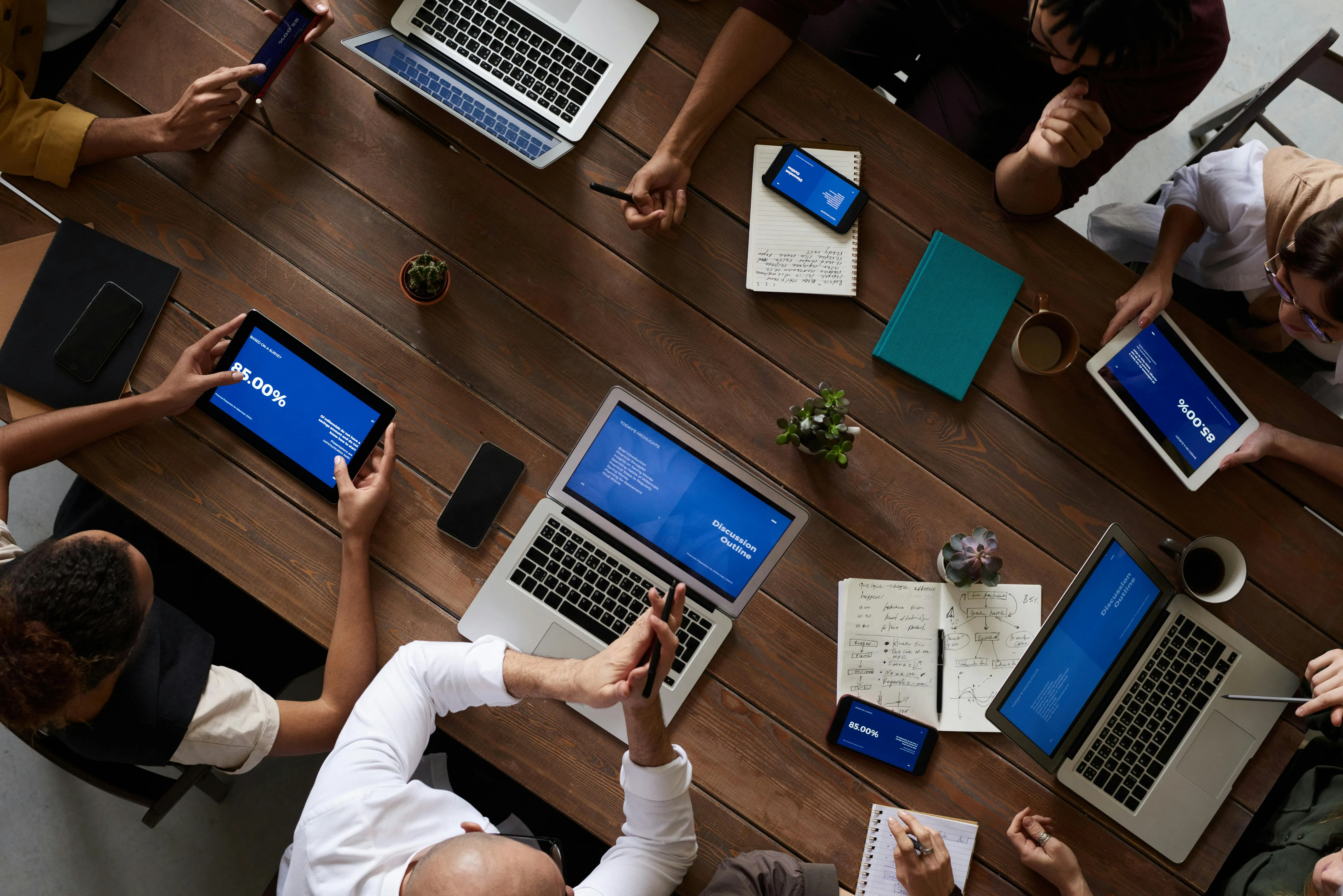 A photo taken from above showing a meeting table with people woriking with their laptops.