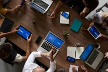 A photo taken from above showing a meeting table with people woriking with their laptops.
